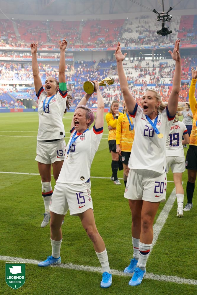Reign standouts Megan Rapinoe (holding trophy) and Allie Long (right) are joined by Alex Morgan in celebrating the United States' successful defense of its World Cup championship in France.(Courtesy John Todd / ISI Photos)