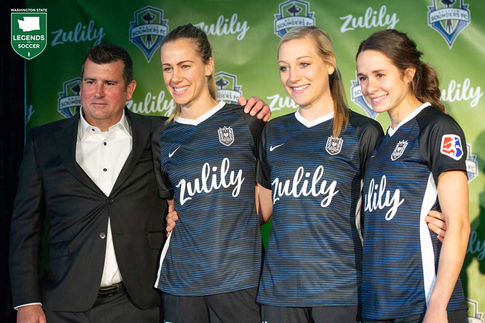 On the move to Tacoma after six seasons in Seattle, Reign FC unveil a revised crest and new jersey sponsor: Zulily. Owner Bill Predmore is joined by (left to right) Beverly Yanez, Megan Oyster and Shea Groom.